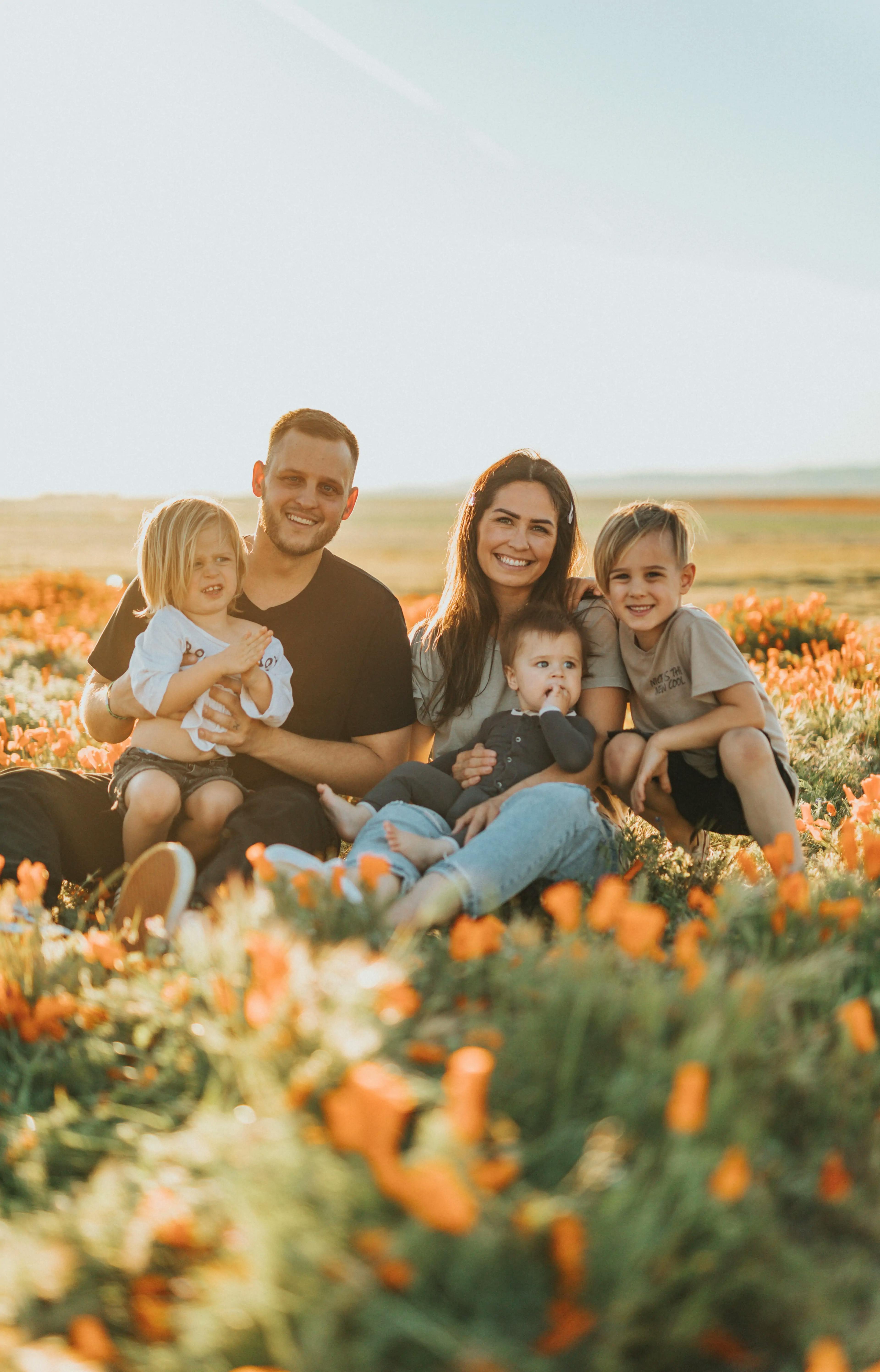Caucasian mother and father with a son, daughter, and infant son, sitting in a field of orange tulips.
